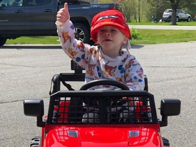 Young boy in toy jeep giving a thumbs up