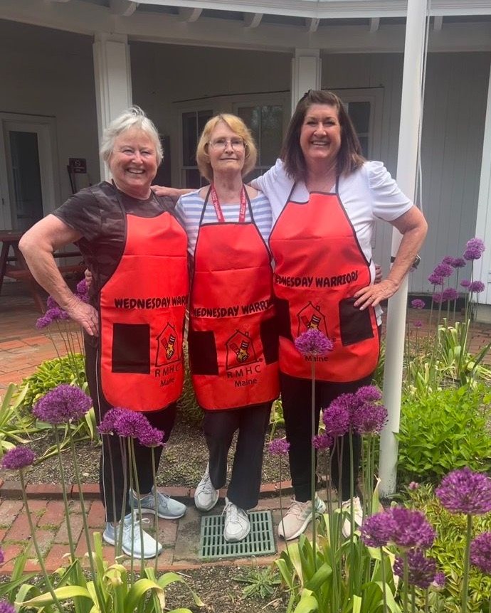 Three volunteers in their homemade 'Wednesday Warriors" aprons stand in the garden of the Portland Ronald McDonald House.