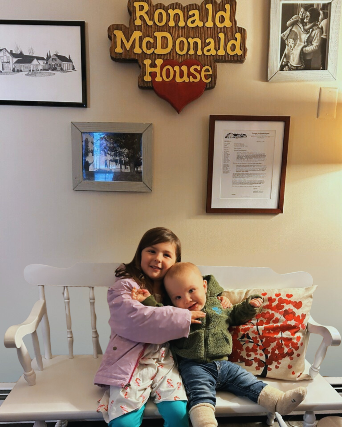Photo of brother and sister sitting on bench in front of Ronald McDonald House sign and other frames
